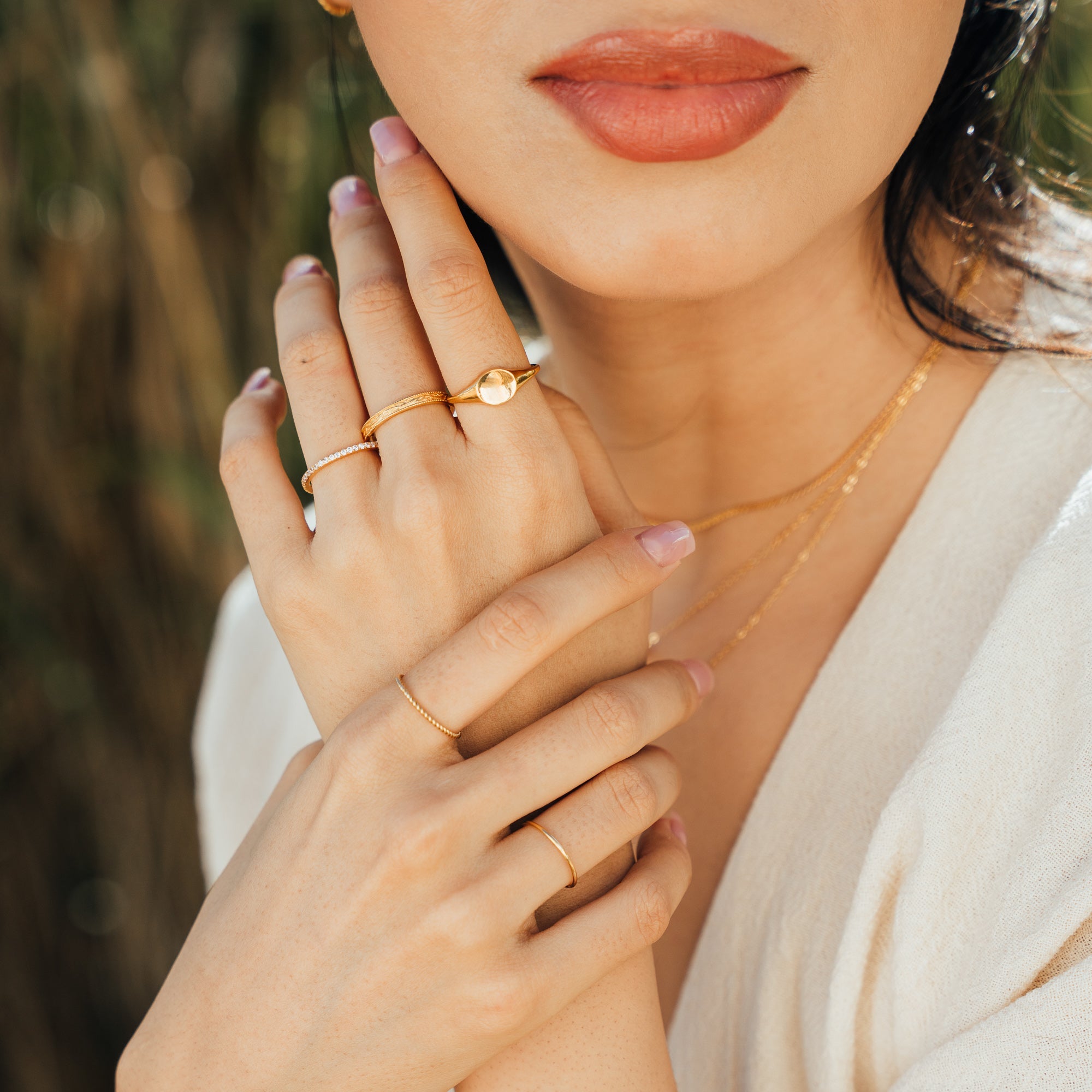 Close-up of a woman’s hands wearing the Dainty CZ Eternity Ring, Round Signet Ring, and Thin Flower Band Ring on one hand, and the Simple Stacking Ring and Dainty Twist Ring on the other.