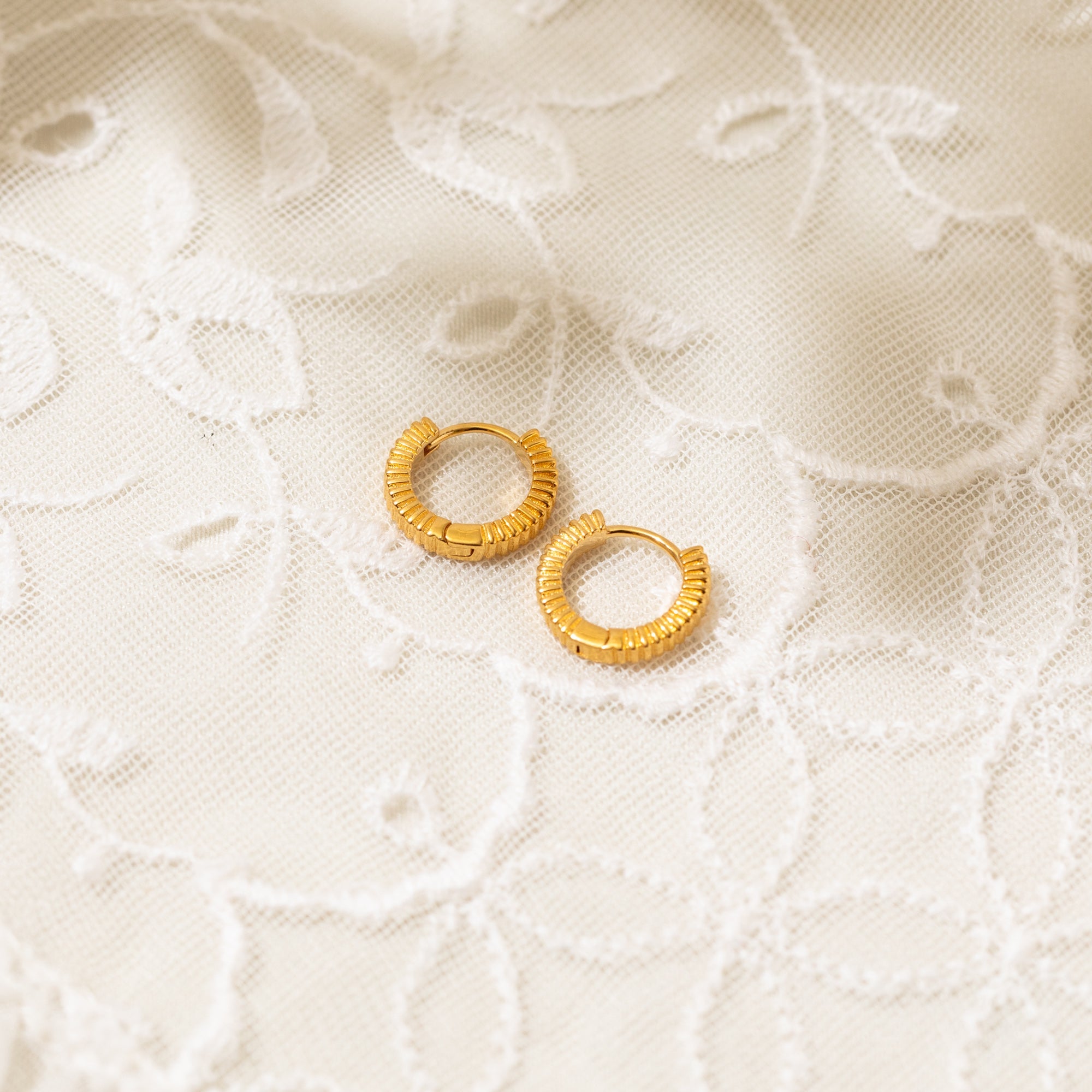 The Ribbed Huggie Hoop Earrings placed on lace fabric.