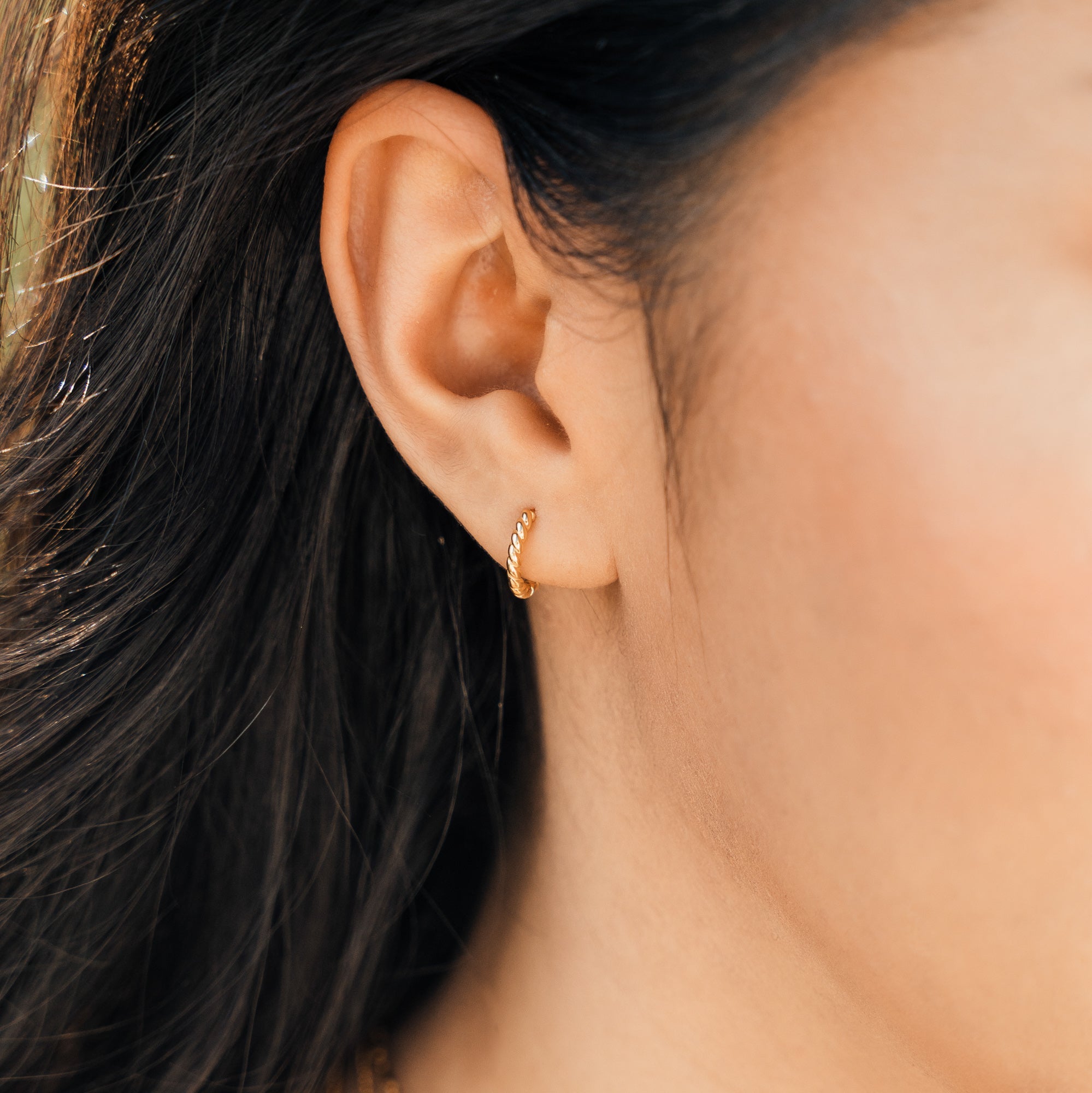 Close-up of a woman’s ear wearing the Rope Huggie Hoop Earrings.